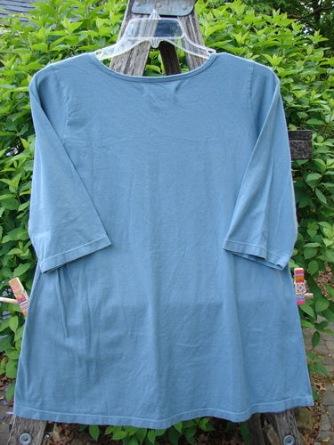 Barclay Three Quarter Sleeved Tee Metallic Belief Spirit Magic Sky Blue Size 1, displayed on a hanger over a wooden ladder, showcases its mid-weight organic cotton with a rounded, rolled neckline and a-line shape.