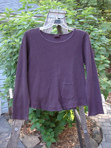 Barclay Patched Thermal Tuck Top Raisin Size 1 displayed on a wooden swing stand, highlighting its lower side tear-shaped pocket, rounded neckline, and longer sleeves.