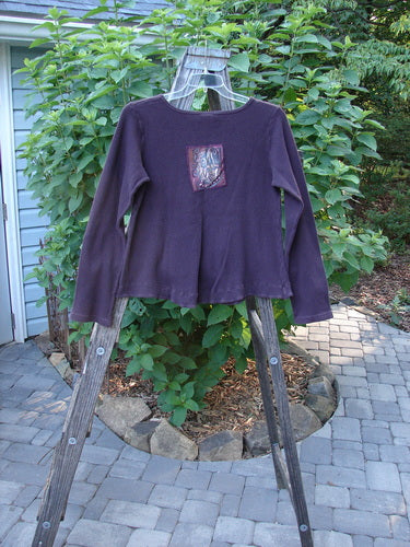 Barclay Patched Thermal Tuck Top Raisin Size 1 displayed on a clothes rack, showcasing its rounded neckline, longer sleeves, banded hemline, lower side pocket, and a teacup patch on the back.