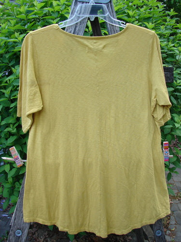 Barclay Slub Short Sleeved Travel Tee Cactus Garden Citron Size 1 hangs on a clear hanger, showcasing its rounded neckline and short sleeves, set against a leafy backdrop, air-drying outdoors.