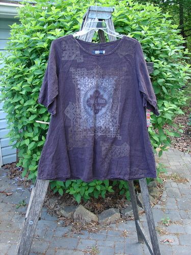 Barclay Linen A Line Top London 1844 Deep Burgundy Size 0, displayed on a wooden ladder, showcases a Celtic-style graphic on the chest, three-quarter sleeves, and a rounded neckline amidst greenery.
