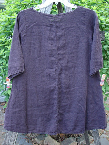 Barclay Linen A Line Top London 1844 Deep Burgundy Size 0, shown outdoors on a hanger, showcases a rounded neckline and slightly flared silhouette amid lush greenery.