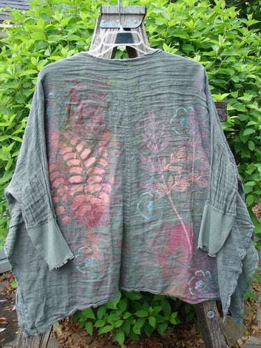 Barclay Crinkle Linen Open Front Rib Sleeve Cheerful Cardigan in Caper, featuring hand-decorated botanical motifs and a unique silhouette, hanging against green shrubbery.