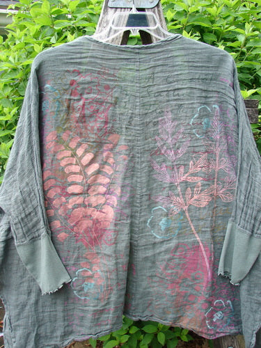 Barclay Crinkle Linen Open Front Rib Sleeve Cheerful Cardigan Scripted Fern Caper Size 0, featuring faded botanical motifs and raw-edged cuffs, hangs outdoors against lush greenery, showcasing its boho-inspired design and generous cut.