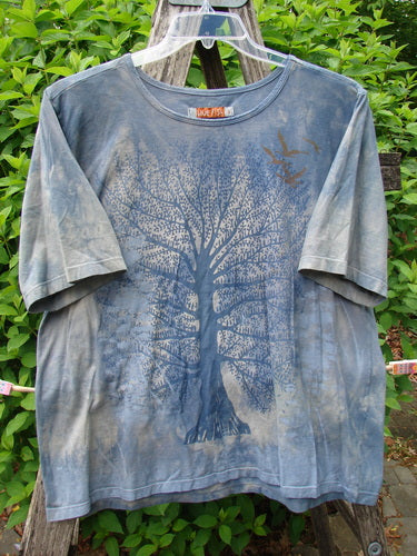 Barclay Fiona Straight Tee Tree Mottled Window Pane Size 0 displayed on a hanger, featuring a stylized tree and bird graphic, draped over a wooden stepladder in an outdoor setting.