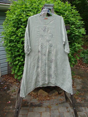 Barclay Linen High Vent Venetian Dress Contour Floral Sage Size 1 displayed outdoors on a wooden ladder, showcasing its oval neckline, three-quarter sleeves, and floral embroidery, highlighting the dress's artistic flair and comfortable design.