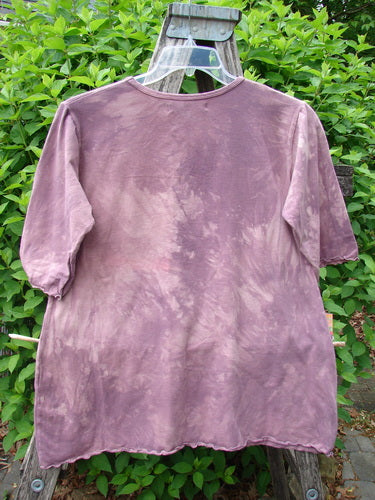 Barclay Cotton Lycra Three Quarter Sleeved Cafe Tee Single Tulip Mottled Mauve Size 1, featuring a tie-dyed pattern, hangs on a plastic hanger over a wooden stepladder against green shrubbery.