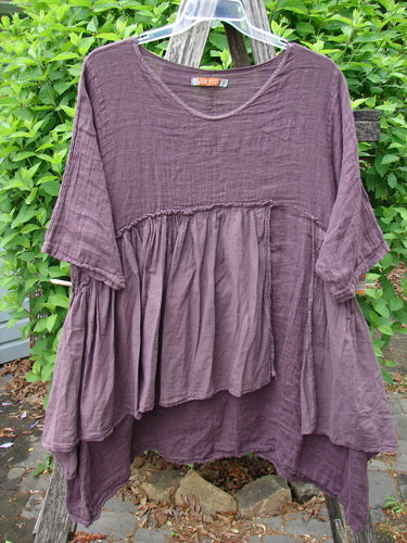 Barclay Gauze Batiste Petal Urchin Flounce Dress Unpainted Fig Size 1: Oversized tunic with a scooped neckline and gathered, tiered lower half, draped on a hanger against green foliage.