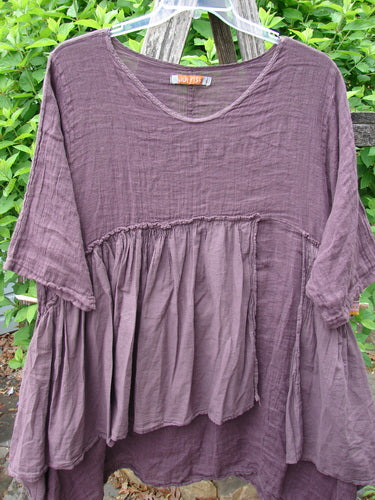 Barclay Gauze Batiste Petal Urchin Flounce Dress Unpainted Fig Size 1: A loose-fitting, long-sleeved tunic with a gathered, layered bodice, hanging against garden greenery, showcasing a flowing, artistic design.