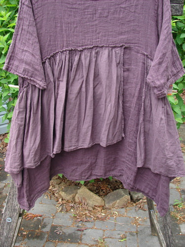 Barclay Gauze Batiste Petal Urchin Flounce Dress Unpainted Fig Size 1: A bohemian-style, crinkled-cotton tunic with a gathered yoke and asymmetrical hem, draped on a wooden ladder outdoors.