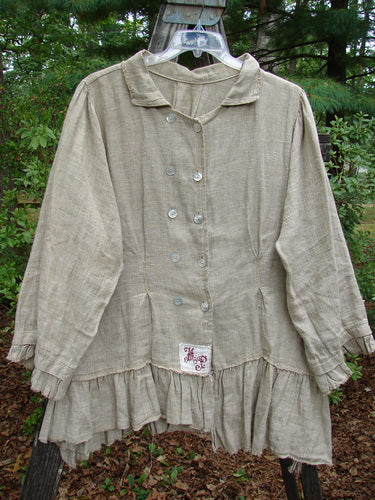 Magnolia Pearl Homespun Linen Double Breasted Curve Jacket displayed on a hanger outdoors. The jacket features a rounded collared neckline, double-breasted buttons, vertical pleats, ruffled hem, and a three-tiered back.