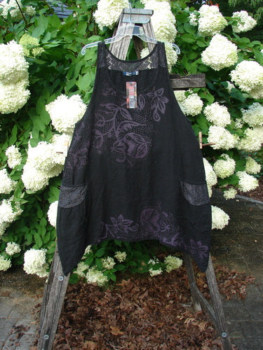 Bluefishfinder.com Barclay NWT Summercloth Lace Two Pocket Pinafore in black, size 0, with a sheer lace overlay and fern floral pattern, two front pockets, and a loose sleeveless A-line shape. It hangs on a wooden stand before white hydrangeas and dense green foliage.