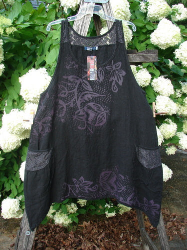 Bluefishfinder.com Barclay NWT Summercloth Lace Two Pocket Pinafore Floral Fern in black, size 0, hangs from a clear plastic hanger with a lace-trimmed neckline, two front pockets, and a sheer floral fern pattern. The lightweight fabric drapes over a rustic ladder against dense green leaves and white blossoms.