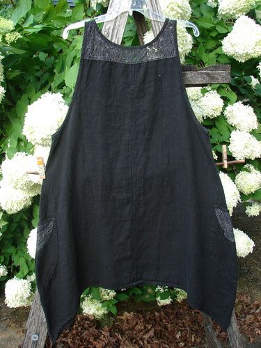 Bluefishfinder.com Barclay NWT Summercloth Lace Two Pocket Pinafore Floral Fern Black Size 0, a black pinafore with a lace-trimmed yoke and two patch pockets. The lightweight fabric hangs in a loose A-line shape, centered on a wooden hanger against dense green foliage and white blossoms.