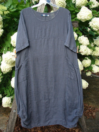 Bluefishfinder.com Barclay Linen Draw Bottom Urchin Dress in unpainted dusty navy, size 0, hangs front-facing with a loose, rounded silhouette and short sleeves. The linen fabric has a soft, textured drape, gathered draw bottom, and side seams that taper into a relaxed, cocoon-like shape.