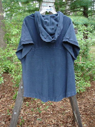 Barclay Celtic Moss Hooded Pocket Cardigan Unpainted Navy Storm Size 0 displayed on a wooden rack, featuring a floppy hood, short sleeves, two pockets, and curly edgings with a full button front.