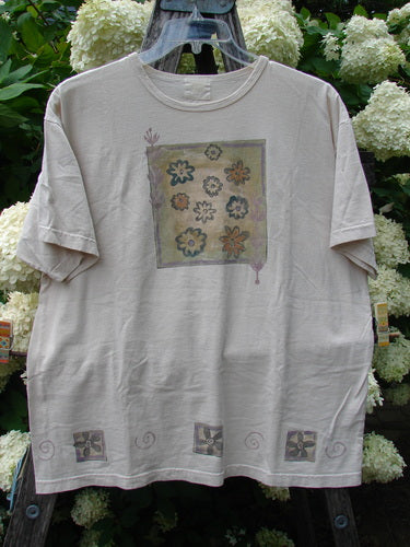Bluefishfinder.com 1999 Short Sleeved Tee Flower Tops Natural Size 1 in a soft natural beige, with a relaxed short-sleeve cut and a faded square floral print centered on the chest. The lightweight tee hangs on a hanger against dense white hydrangeas and dark greenery, with small decorative motifs along the hem.