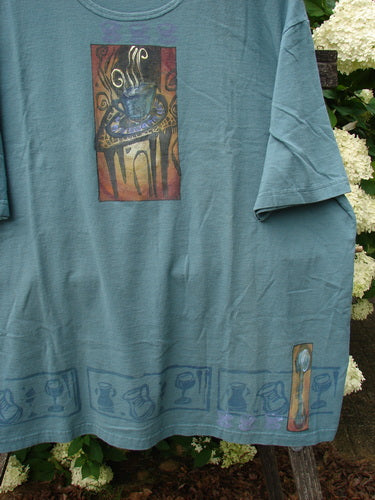 Bluefishfinder.com 2000 Artist Choice short-sleeved tee in green mineral, with a relaxed crew neck and soft, slightly wrinkled cotton knit. A steaming teacup graphic sits centered on the chest, while a muted border of teacups runs along the hem.