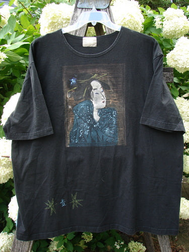 Bluefishfinder.com 1999 Short Sleeved Tee Geisha Gal Black Size 2 in black cotton, with a faded rectangular geisha portrait centered on the chest and small green graphic accents near the hem. The short sleeves and worn, matte finish give it a vintage look.