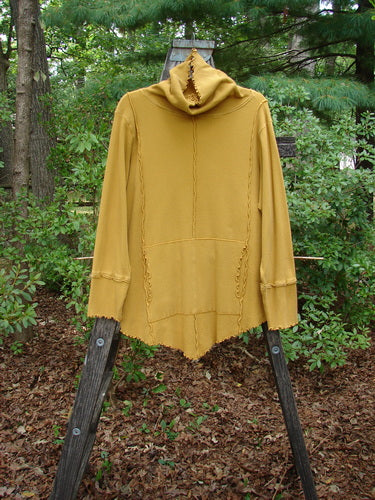 Barclay Thermal Reverse Stitch Tunnel Pocket Top Unpainted Mustard Size 1 displayed on a wooden stand, showing its unique floppy turtleneck, center drop pocket, and exterior stitched vertical seams.