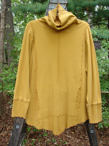 Barclay Thermal Reverse Stitch Tunnel Pocket Top displayed on a wooden pole, showcasing its curly cowl neck, kangaroo pocket, and hourglass shape, with exterior stitched seams and a unique drape.