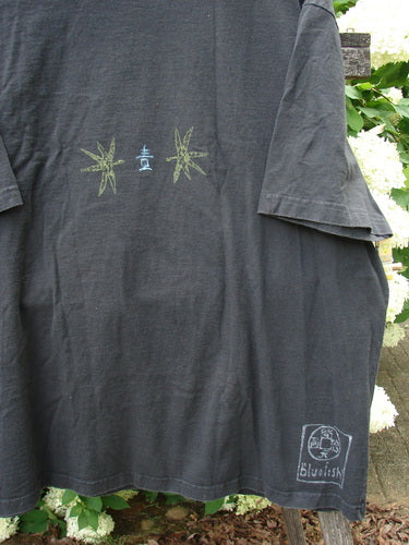 Bluefishfinder.com 1999 Short Sleeved Tee Geisha Gal Black, a faded black T-shirt with short sleeves, a small centered geisha graphic, and a Bluefish logo at the lower hem. The soft, worn cotton hangs loosely against a leafy outdoor backdrop.