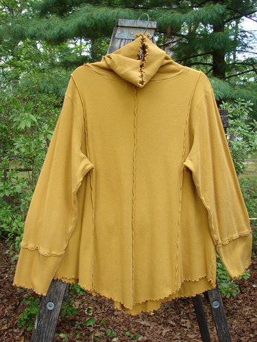 Barclay Thermal Reverse Stitch Tunnel Pocket Top displayed on a wooden pole, showcasing its unique turtleneck, kangaroo pocket, and exterior stitched seams in a slightly hourglass shape, with varying hemlines.