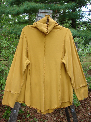 Barclay Thermal Reverse Stitch Tunnel Pocket Top Unpainted Mustard Size 1 displayed on a tree stump, showcasing its unique curly turtleneck, central kangaroo pocket, and exterior stitched vertical seams.