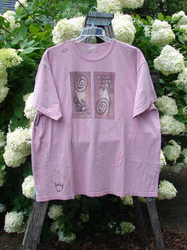 Bluefishfinder.com 1999 Short Sleeved Tee Double Daisy Peony Size 2 in faded lavender cotton, with a relaxed short-sleeve cut and two muted floral panel prints on the chest. The tee hangs from a wooden stand before dense white hydrangeas and green foliage, creating a soft, natural backdrop.