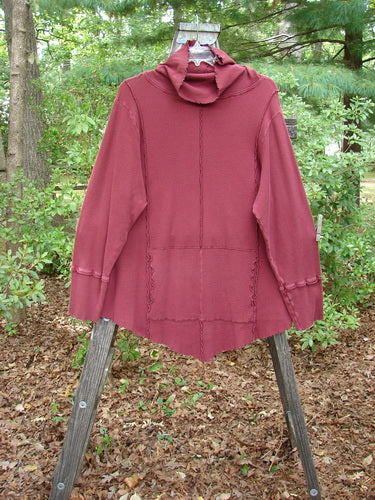 Barclay Thermal Reverse Stitch Tunnel Pocket Top Unpainted Burgundy Size 2 displayed on a wooden stand, featuring a turtleneck, center front pocket, and unique hourglass shape with varying hemline.