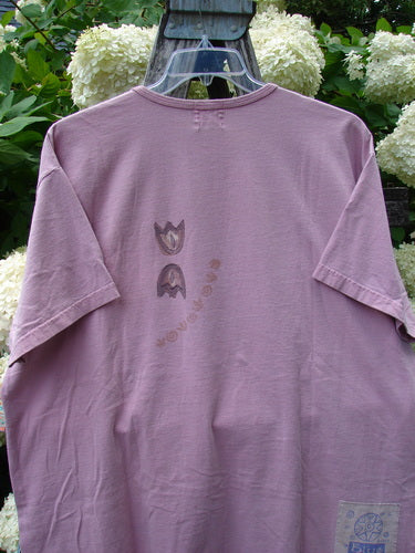Bluefishfinder.com 1999 Short Sleeved Tee Double Daisy Peony Size 2 in dusty mauve, a short-sleeved T-shirt with a soft, worn cotton look and a small centered floral graphic. It hangs on a clear hanger, with white hydrangeas and green foliage behind it.