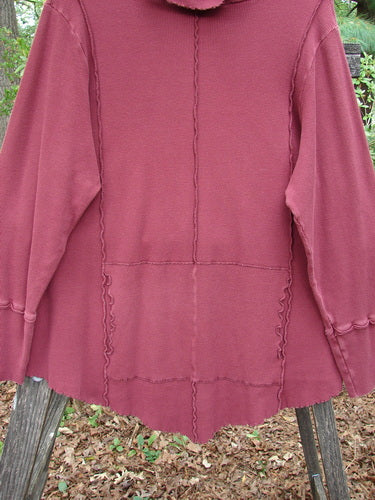 Barclay Thermal Reverse Stitch Tunnel Pocket Top in Burgundy on a wooden stand, showcasing a curly-edged turtleneck, center front kangaroo pocket, and exterior stitched seams, highlighting its unique cut and drape.