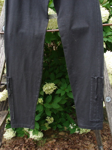 Bluefishfinder.com Barclay Cotton Lycra Side Gather Legging in unpainted black, size 0, shown as slim black leggings with gathered side seams and narrow leg openings. The cotton-lycra fabric has a smooth, matte finish, hanging against leafy greenery in soft natural light.