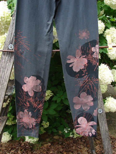 Bluefishfinder.com Barclay Cotton Lycra Legging Daisy Twig Off Black Size 0 in off-black cotton Lycra, with a slim straight-leg silhouette and pink daisy-and-twig print down the lower legs. The leggings hang outdoors against leafy greenery and white flowers, with soft natural light flattening the dark matte fabric.