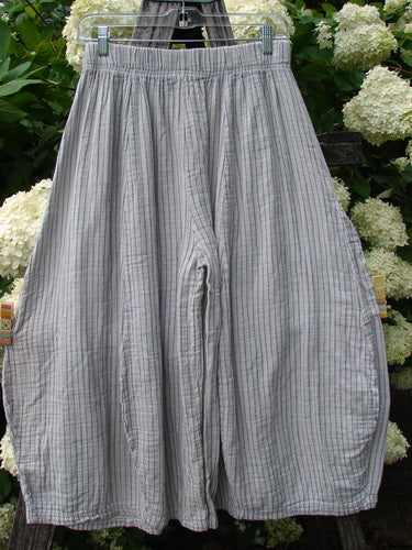 Bluefishfinder.com Barclay Gauze Crop Mojo Pant in unpainted sandy stripe, size 0, shown as loose gray gauze crop pants with a gathered elastic waist, wide rounded legs, and fine vertical striping. The lightweight, crinkled fabric hangs from a hanger against leafy white flowers.