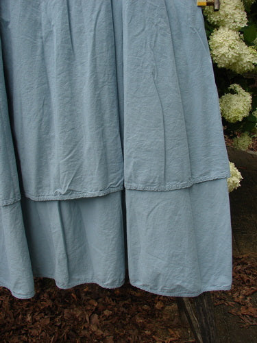 Bluefishfinder.com Barclay Batiste Fold Over Two Tier Stardust Skirt in unpainted dusky sky, a soft blue tiered skirt with a folded-over waistband and gently crinkled batiste texture. The layered hem falls in two airy panels, with flowers and dark ground softly framing the lower edge.