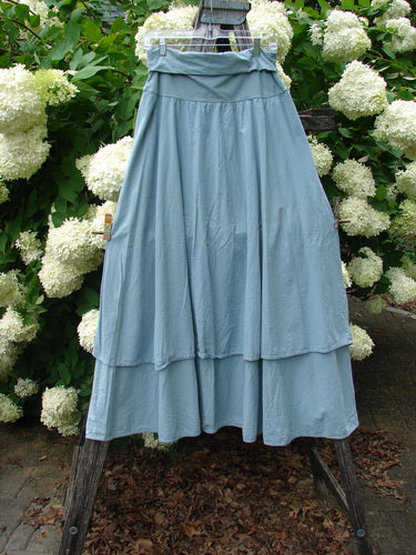 Bluefishfinder.com Barclay Batiste Fold Over Two Tier Stardust Skirt in unpainted dusky sky, a light blue, two-tier skirt with a folded-over waistband and soft batiste texture. It hangs full and draped against white hydrangeas, with a matte, airy finish.