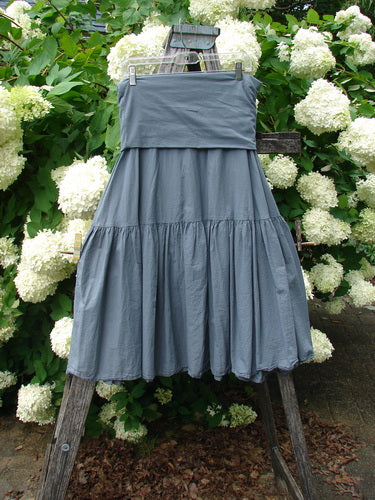 Bluefishfinder.com Barclay Linen Fold Over Single Tier Trinity Skirt, size 0, in unpainted diatom gray linen. The skirt hangs from a rustic wooden ladder, with a folded-over waistband, a single gathered tier, and a softly textured, full drape set against white hydrangeas and green foliage.
