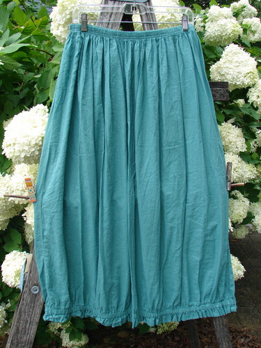 Bluefishfinder.com Barclay Batiste Airy Lawn Skirt in unpainted jade, size 0, hangs from a clear clip hanger in a full, softly gathered silhouette. The lightweight lawn fabric shows a fine, airy texture and a gently crinkled drape, set against dense green foliage and white hydrangea blooms.