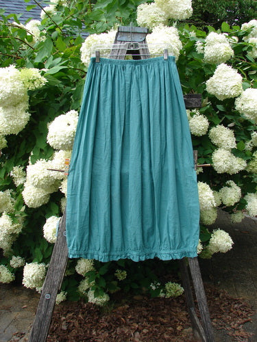 Bluefishfinder.com Barclay Batiste Airy Lawn Skirt in unpainted jade, size 0, hangs from a rustic wooden ladder against dense white hydrangea blooms. The lightweight lawn fabric falls in soft vertical pleats with a gently gathered waist and a narrow hem.