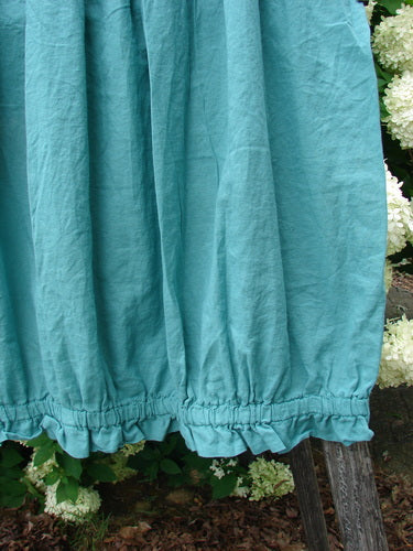 Bluefishfinder.com Barclay Batiste Airy Lawn Skirt in unpainted jade, size 0, with a softly gathered hem and lightweight crinkled lawn texture. The teal fabric hangs in loose vertical folds, filling the frame against leafy garden greenery.