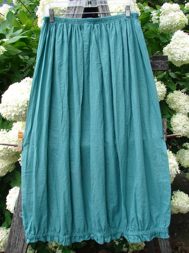 Bluefishfinder.com Barclay Batiste Airy Lawn Skirt in unpainted jade, size 0, with a gathered elastic waist and long, softly pleated silhouette in lightweight woven fabric. It hangs against dense white hydrangeas and dark wood, creating a cool teal-green contrast.