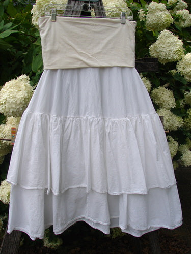Bluefishfinder.com Barclay Linen Fold Over Two Tier Trinity Skirt in unpainted white, Size 0, with a wide folded linen waistband and two tiered, softly gathered cotton layers. The skirt hangs from clips against leafy hydrangeas, with a bright, airy palette and textured fabric folds.