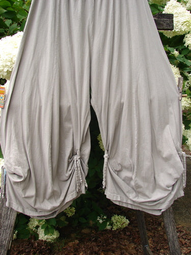 Bluefishfinder.com Barclay Crop Tie Bottom Crop 4 Square Pant in unpainted sand cloud, size 0, with wide draped legs and tied hems in soft, lightweight-looking fabric. The pale neutral pants hang front and center against leafy greenery, creating a loose, airy silhouette.