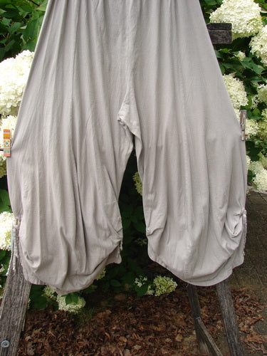 Bluefishfinder.com Barclay Crop Tie Bottom Crop 4 Square Pant in unpainted sand cloud, size 0, shown as loose, draped cropped pants with gathered tie hems and a soft matte finish. The pale gray-beige fabric hangs in rounded folds, framed by greenery behind it.