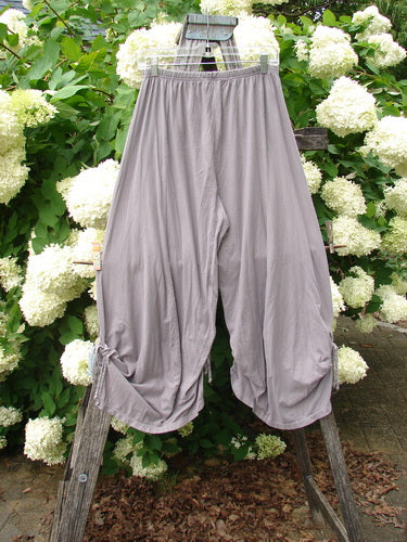 Bluefishfinder.com Barclay Crop Tie Bottom Crop 4 Square Pant in unpainted plum cloud, size 0, shown as loose gray-lavender cropped pants with a gathered elastic waist, wide draped legs, and tie hems, hanging against white hydrangeas and green foliage.