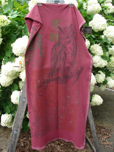 Bluefishfinder.com Barclay Heavy Weight Organic Sweatshirt Blanket Owl Forest Trimmed Burgundy OSFA, a burgundy blanket with a large owl-and-forest graphic and trimmed edges, draped vertically over a wooden stand. The heavy fabric shows a soft sweatshirt-like texture against white hydrangeas and green foliage.