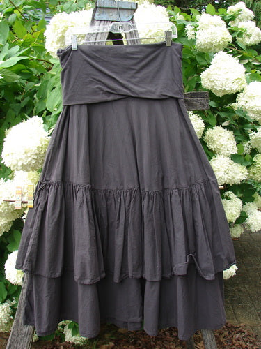 Bluefishfinder.com Barclay Linen Fold Over Two Tier Trinity Skirt Unpainted Brum Size 0 in dark charcoal linen, with a wide folded-over waistband and two tiered, softly gathered panels. The skirt hangs from a wooden ladder amid white hydrangeas, its matte texture and layered drape standing out against the lush green garden backdrop.
