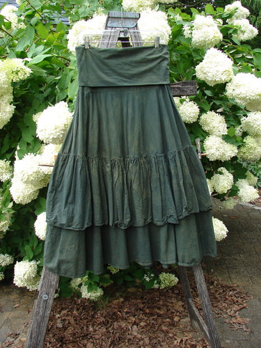 Bluefishfinder.com Barclay Linen Fold Over Two Tier Trinity Skirt, unpainted mottled army size 0, hangs from a wooden ladder amid white hydrangea blooms. The dark green linen has a folded waistband and two tiered, softly gathered layers with a textured, matte finish.