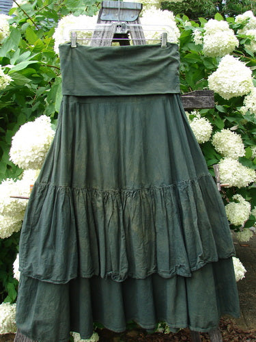 Bluefishfinder.com Barclay Linen Fold Over Two Tier Trinity Skirt in unpainted mottled army, a dark green linen skirt with a folded waistband and two tiered ruffled layers. It hangs centered from a clip hanger, its softly crinkled texture set against white hydrangeas and leafy greenery.